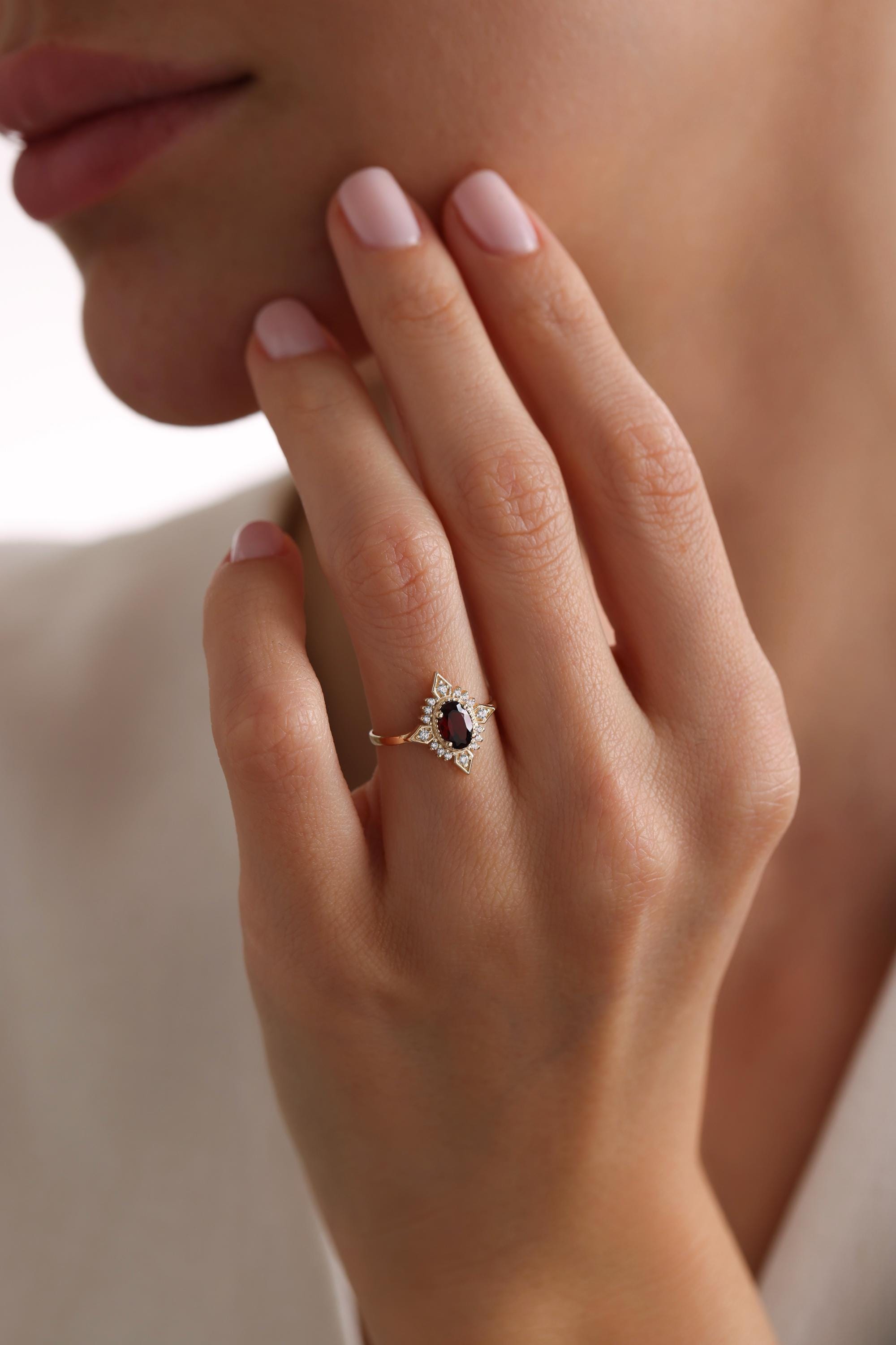 May include: A gold ring with a red oval gemstone surrounded by smaller white gemstones.