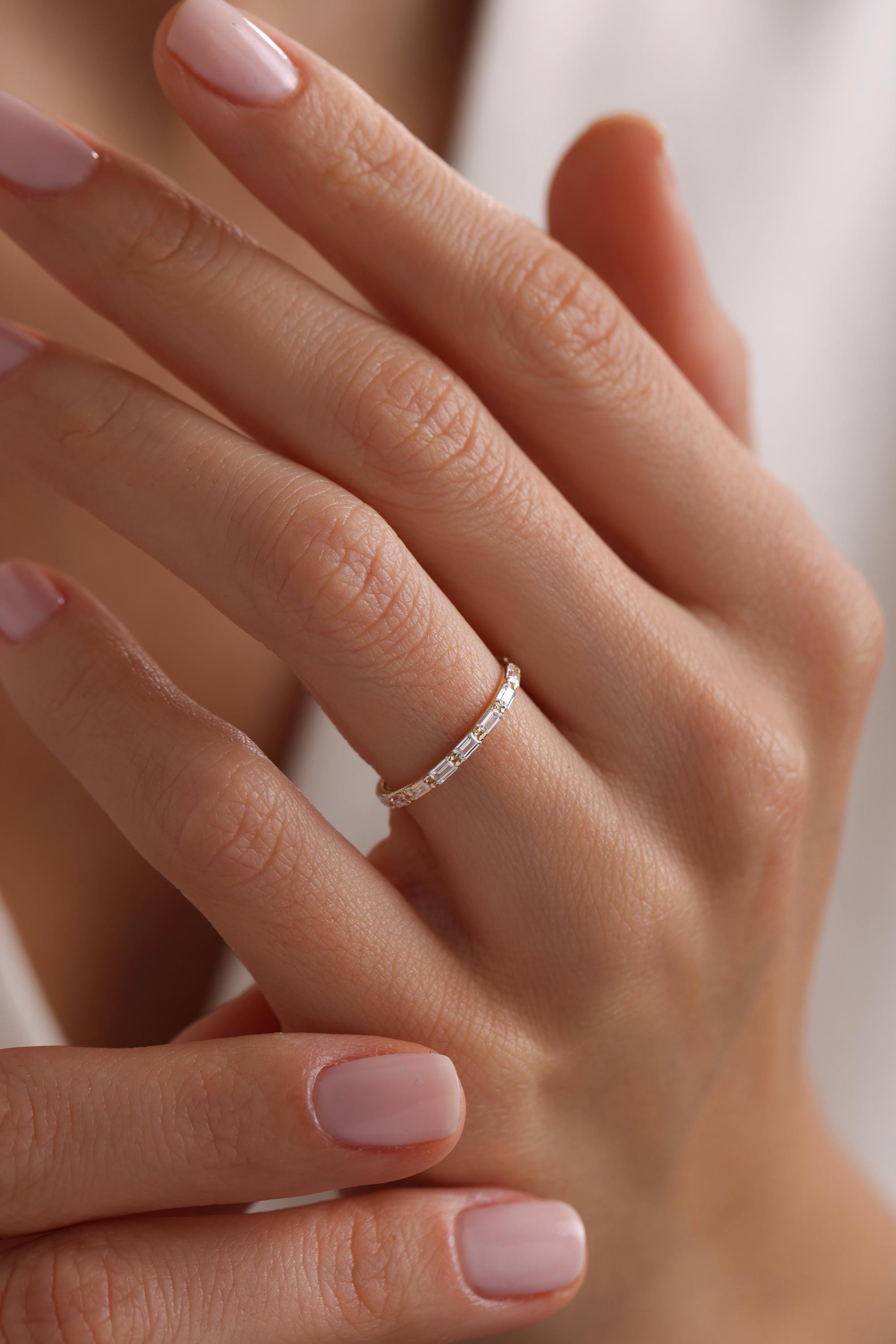 May include: A thin gold band with a row of small, rectangular, clear gemstones.