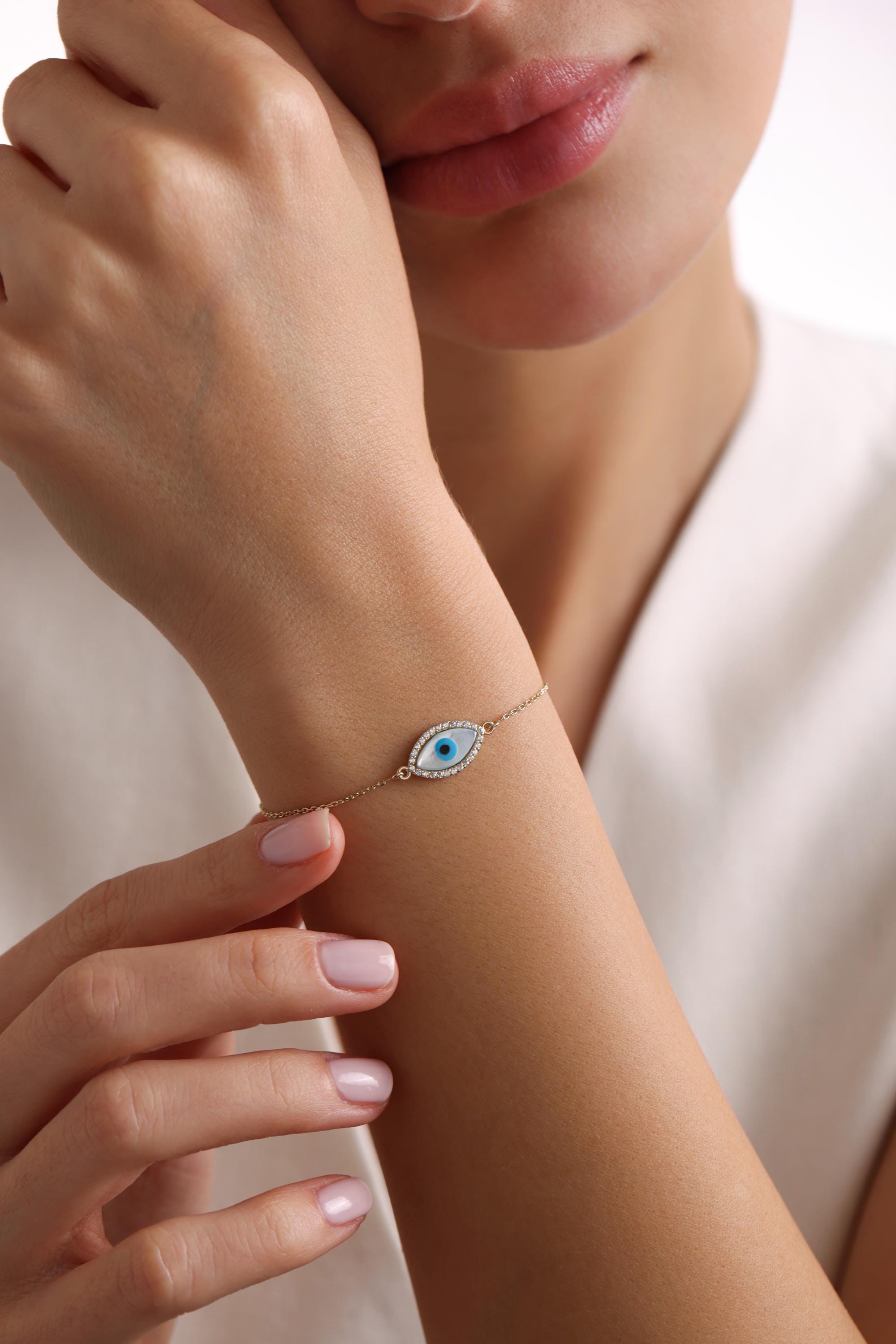 May include: A gold chain bracelet with a blue and white evil eye charm. The charm is surrounded by small diamonds.