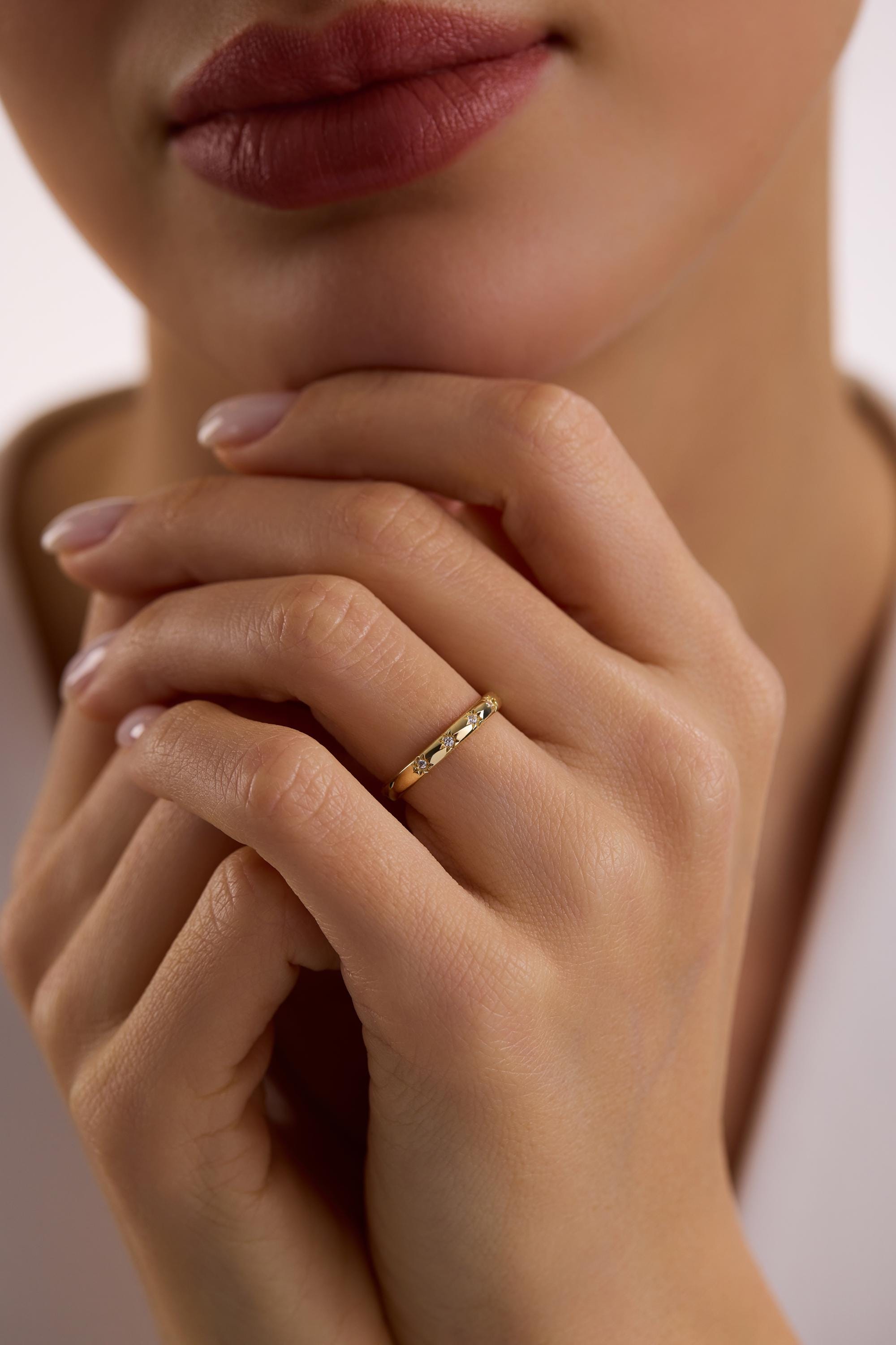 May include: A gold ring with small, clear gemstones set along the band. The ring is on a person's finger, with the hand in focus. The ring appears to be a wedding band or a similar style of jewelry.