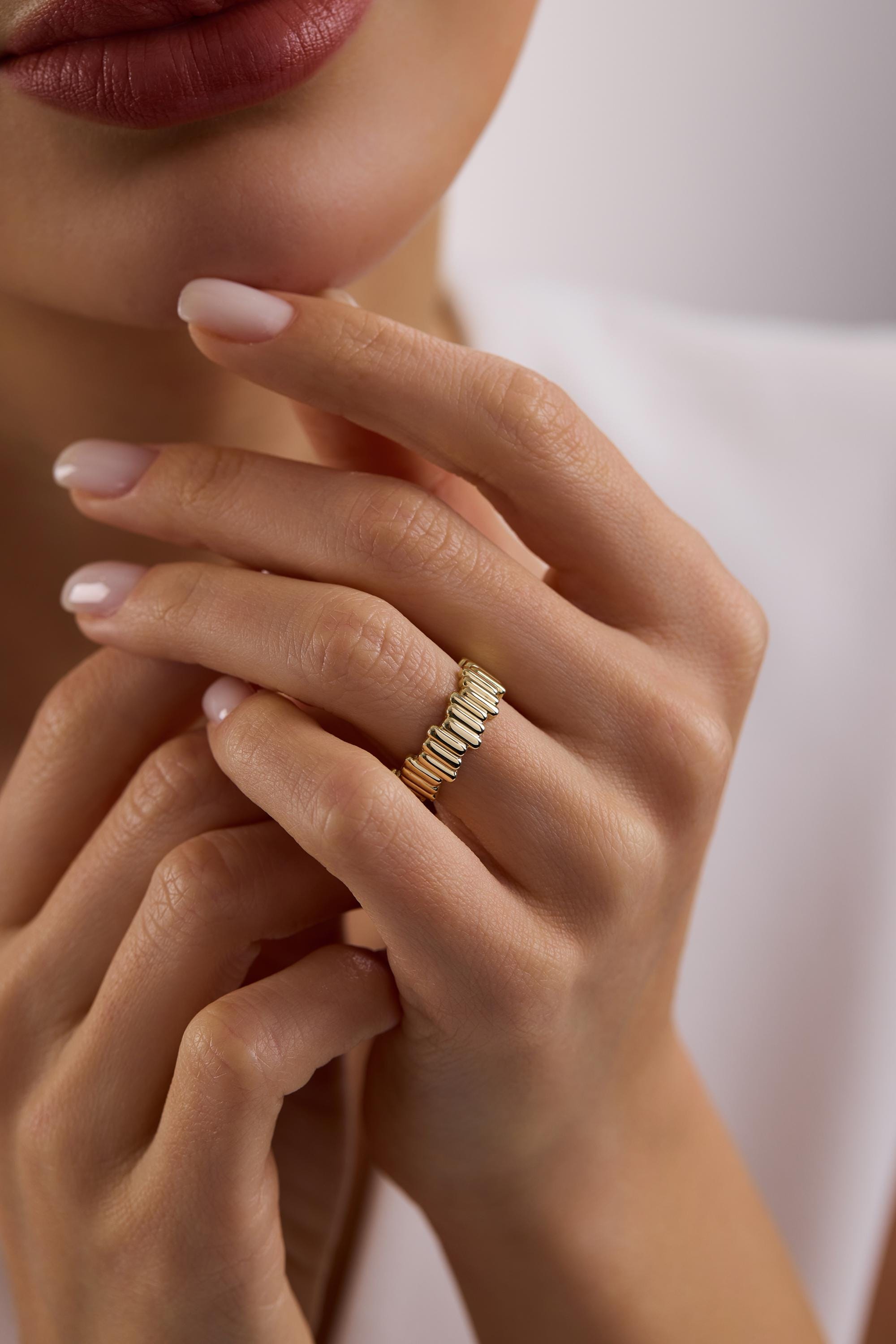 May include: A gold-colored ring with a ribbed design. The ring is worn on a finger. The ring's design features vertical lines, creating a textured appearance. The ring is a simple yet elegant piece of jewelry.