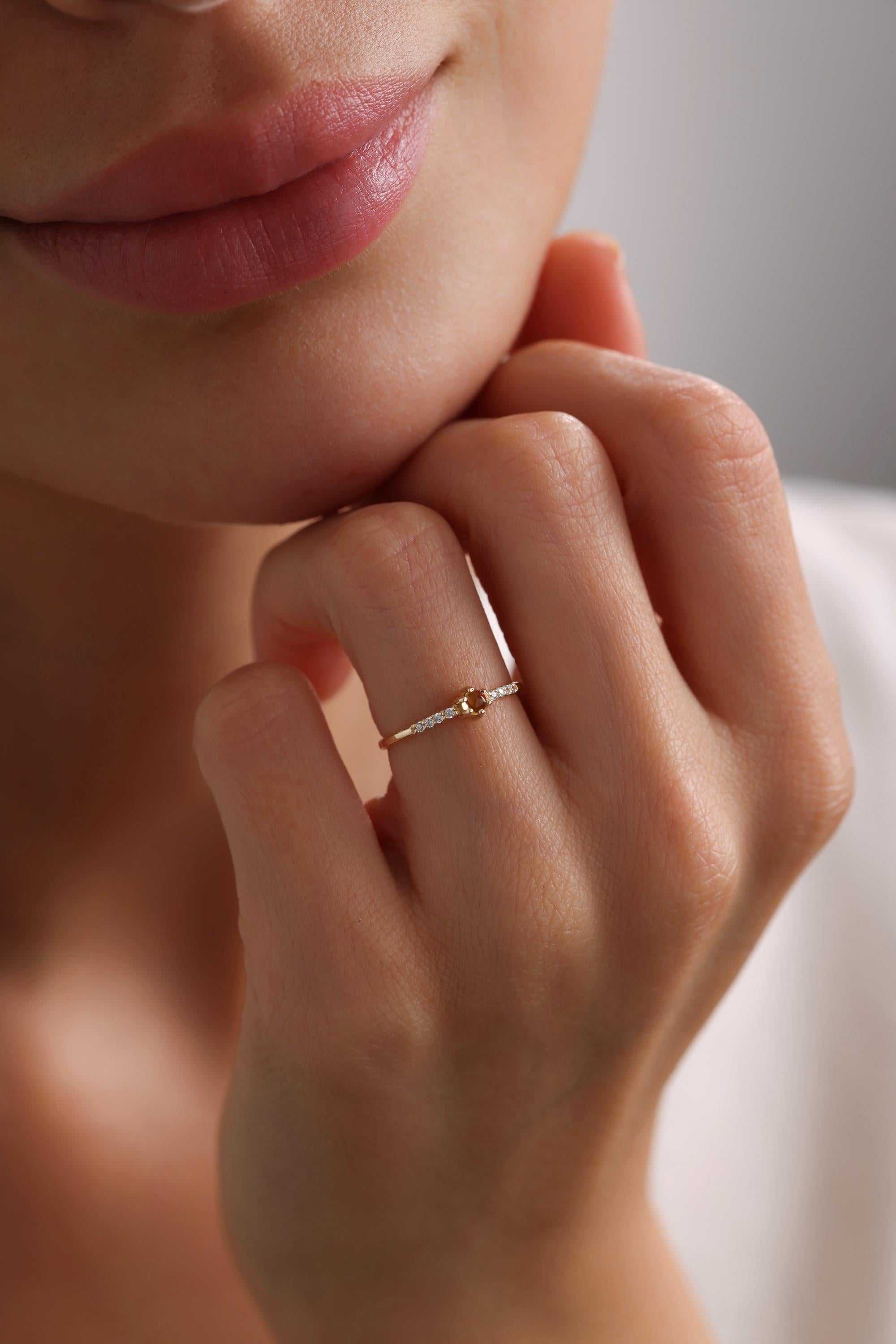 May include: A delicate gold ring with a small round gemstone in the center and a row of small diamonds on each side.