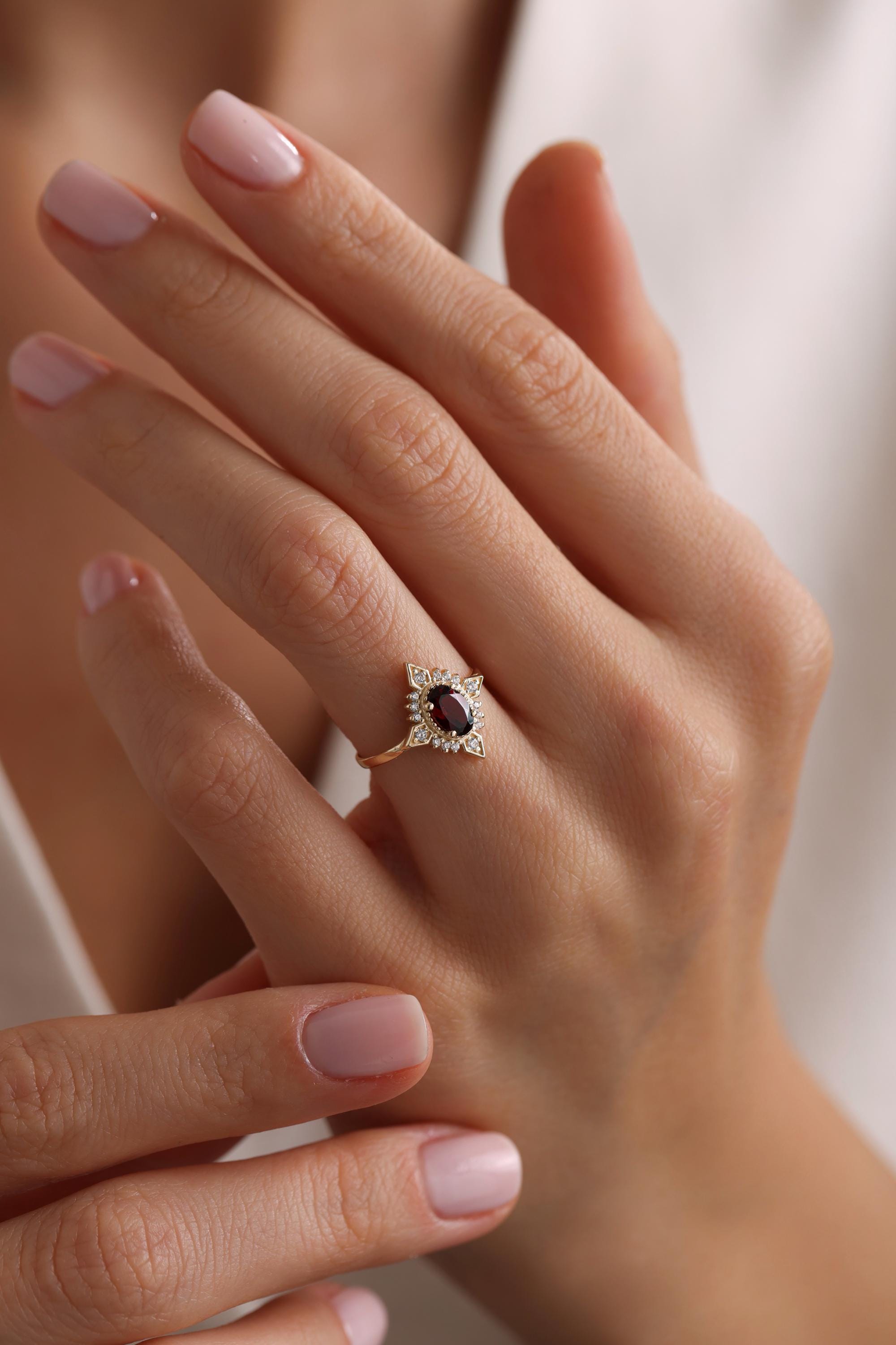 May include: A gold ring with a red oval gemstone surrounded by smaller white gemstones.
