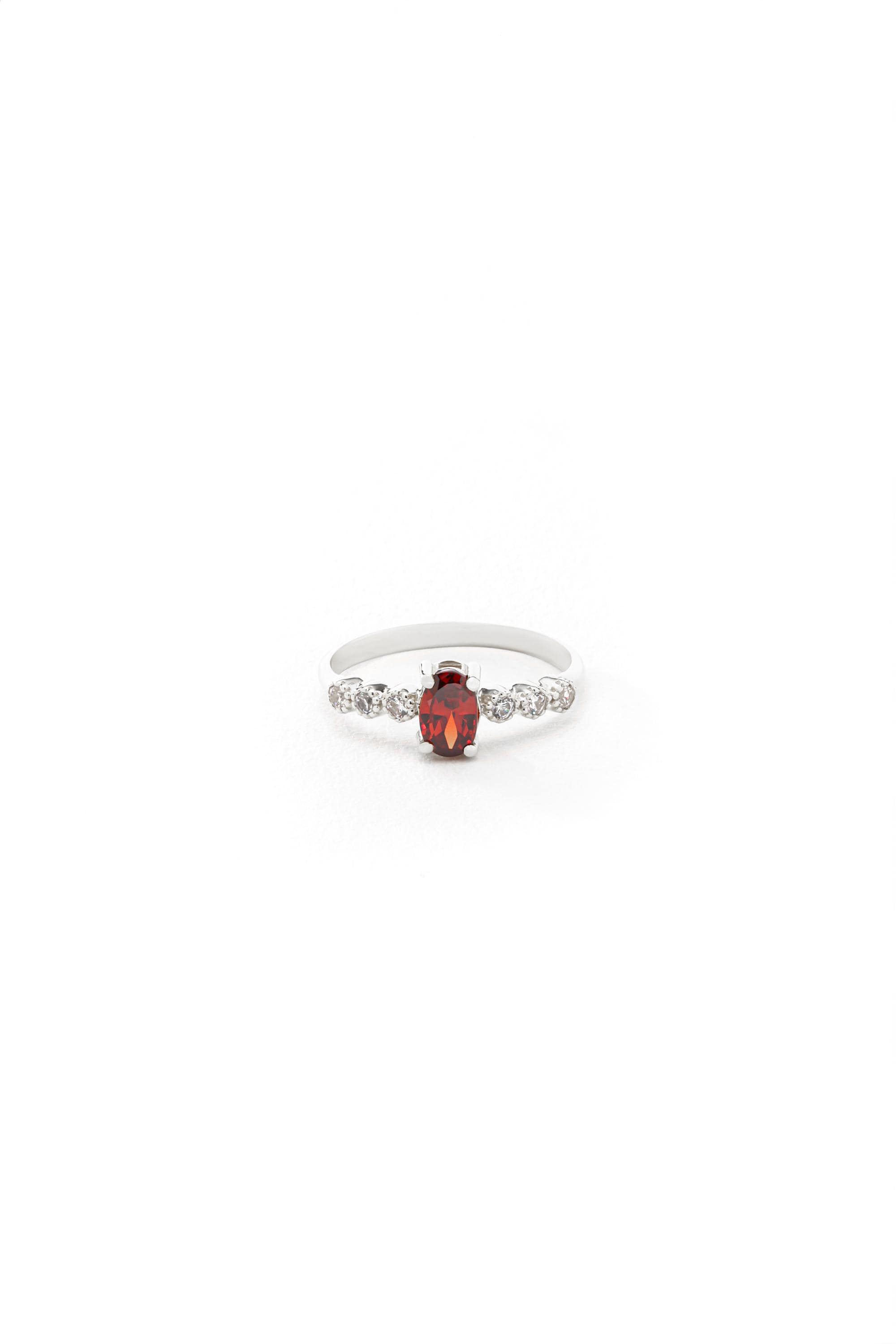 A silver ring with a red gemstone, possibly a garnet, set in a band of smaller diamonds.