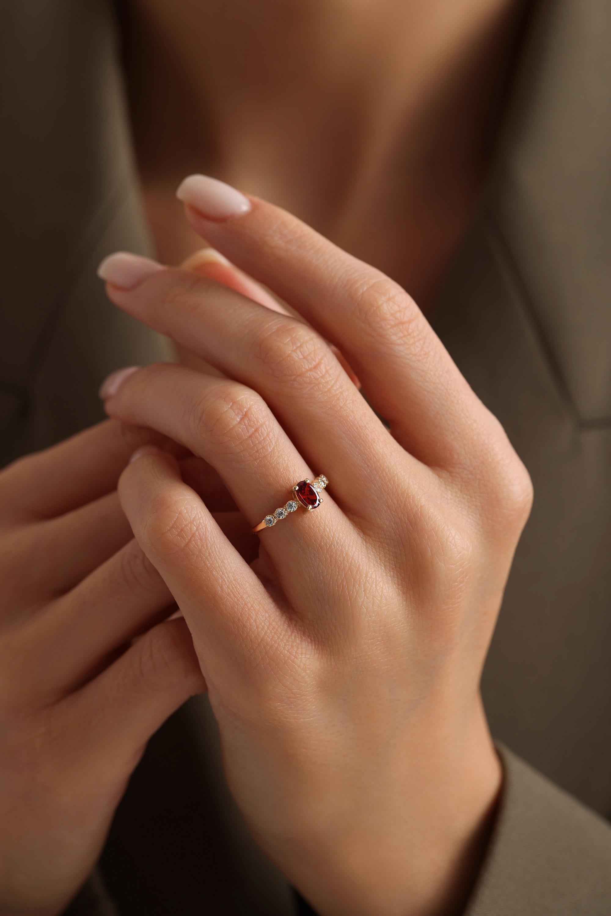 A close-up of a person's hand wearing a gold ring with a red gemstone.