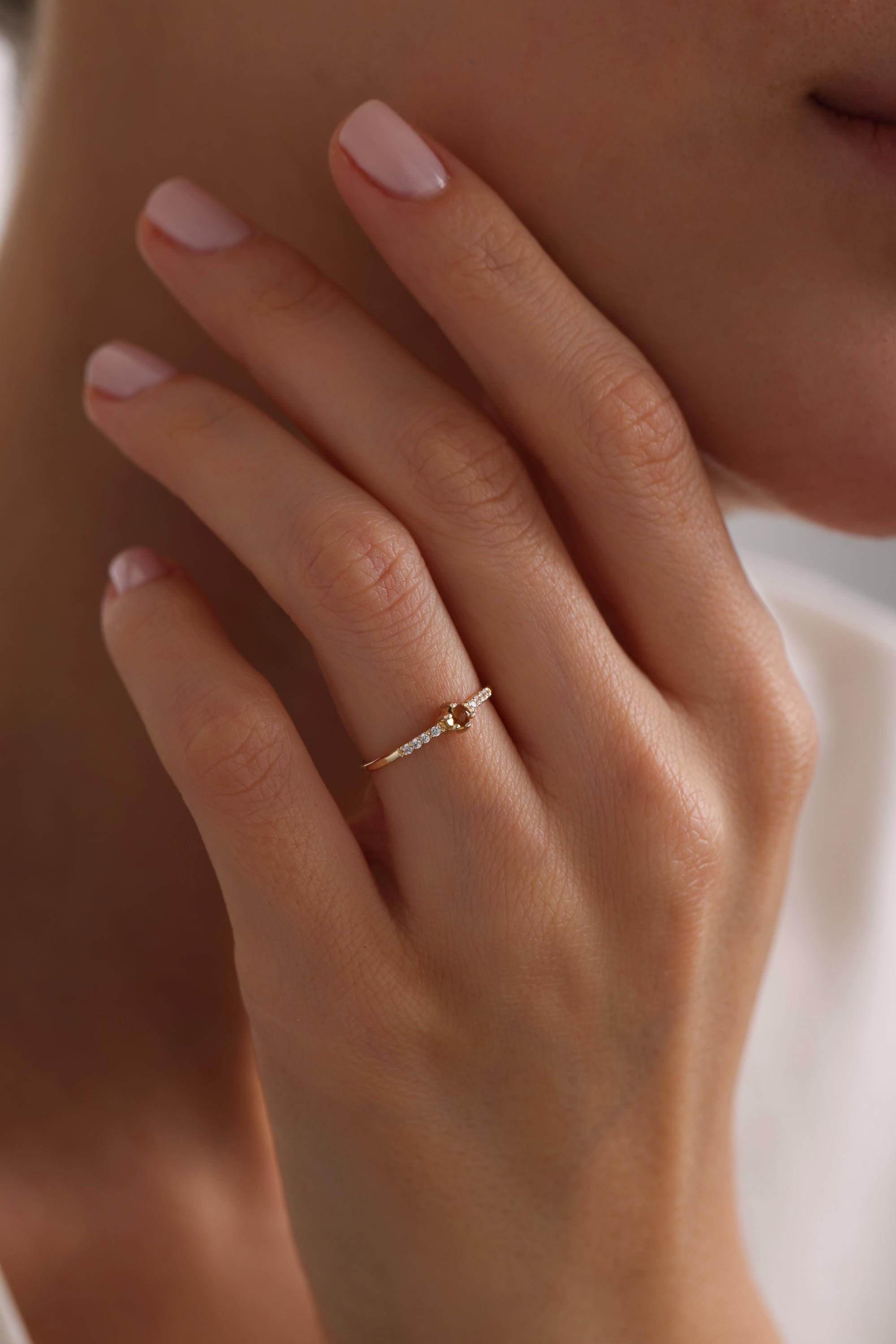 May include: A gold ring with a single, round, brown gemstone and smaller, clear gemstones set in a curved band.