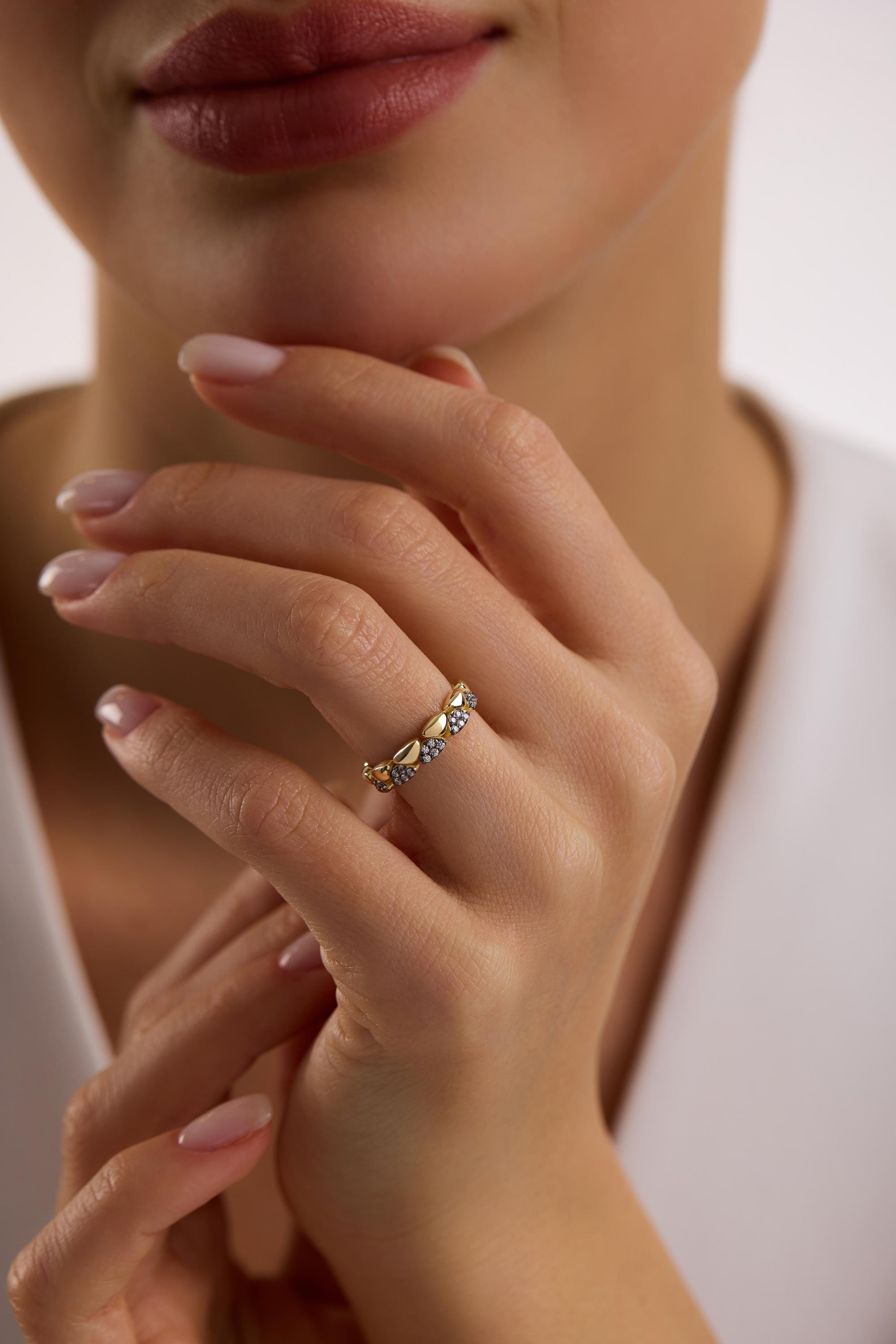May include: A gold ring with a repeating heart and small stone design. The ring is worn on a person's finger. The ring is a bright gold color and the small stones are a light blue color.