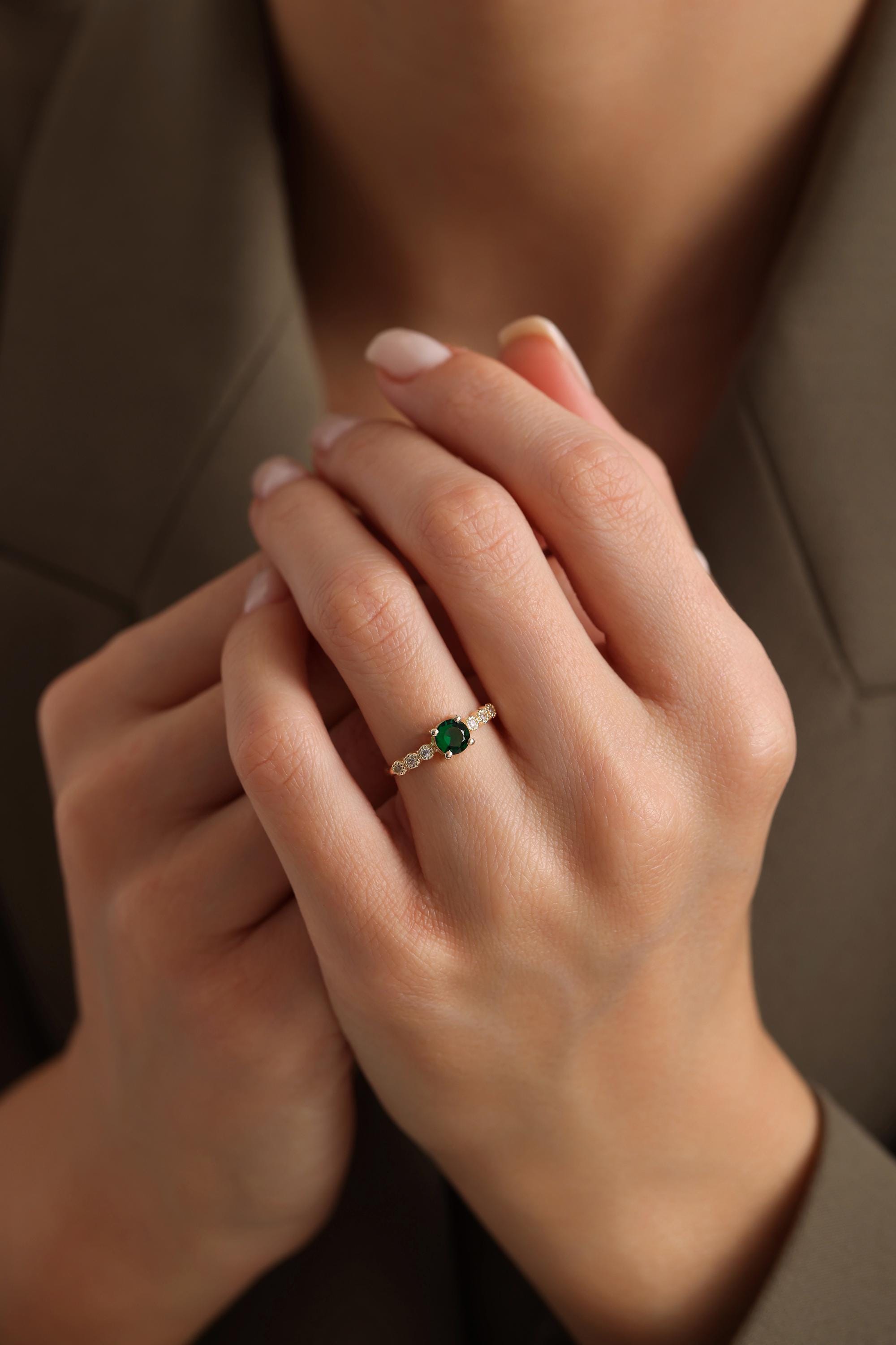 May include: A gold ring with a green gemstone and small white gemstones around the band.