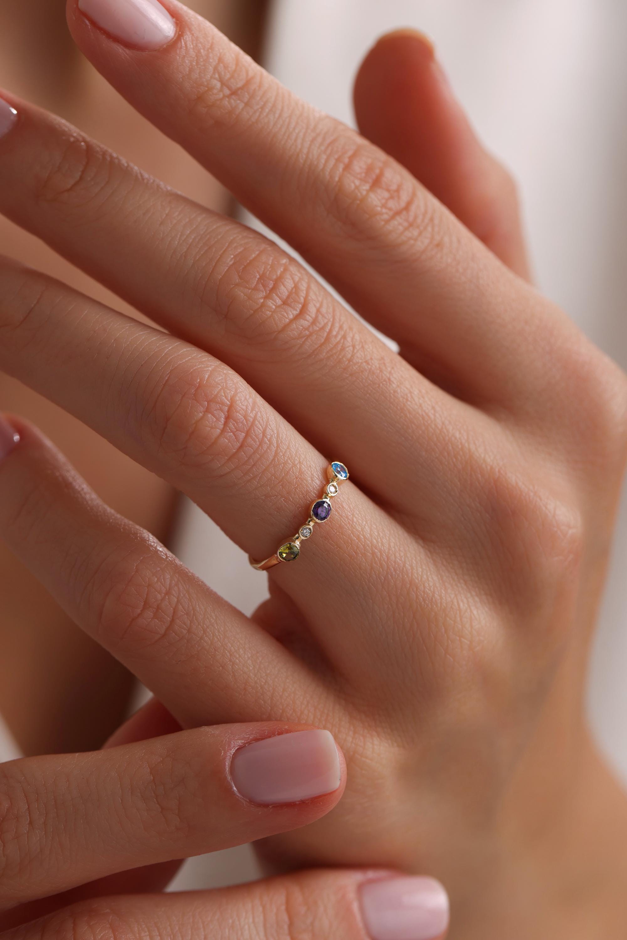 May include: A gold band ring with a row of colorful gemstones. The gemstones are blue, green, yellow, and white.