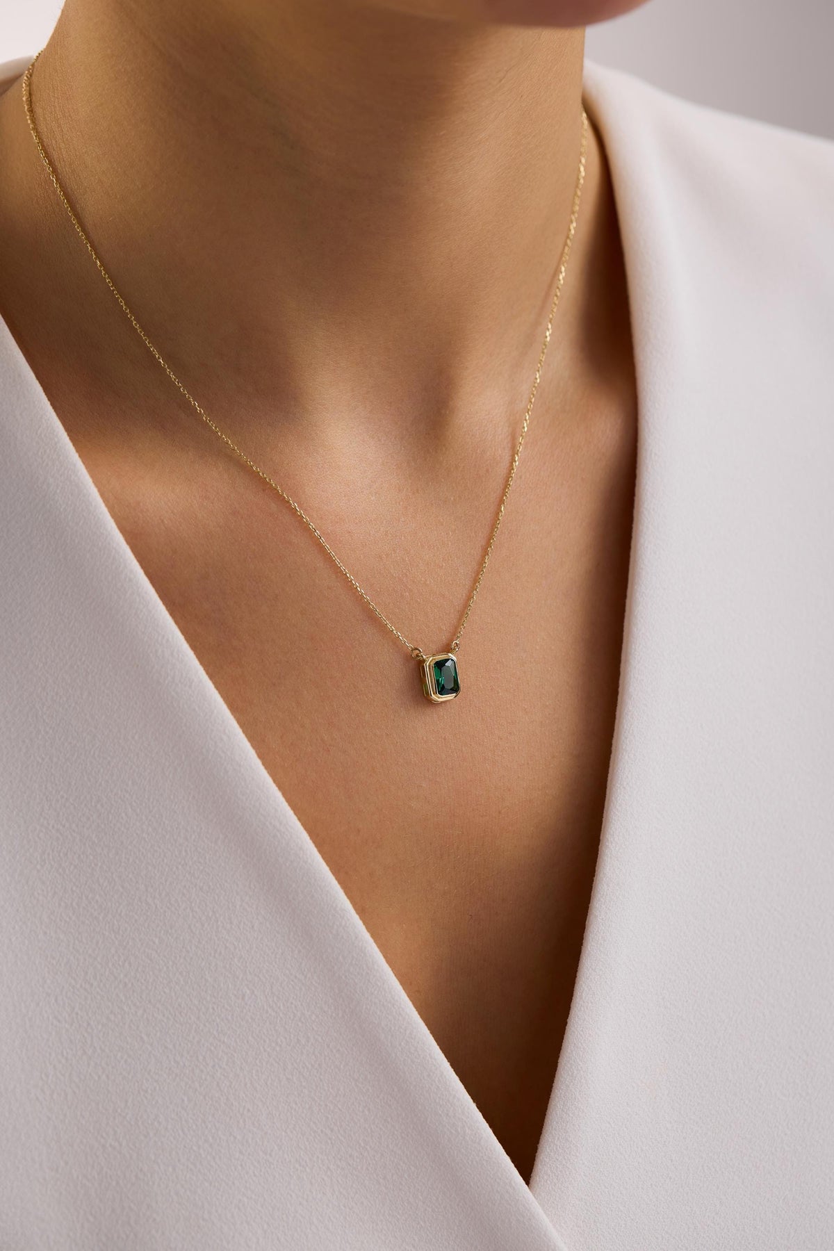 May include: A gold necklace featuring a square, emerald-cut, dark green gemstone pendant. The pendant is set in a gold bezel and hangs from a delicate gold chain. The necklace is displayed against a white background.