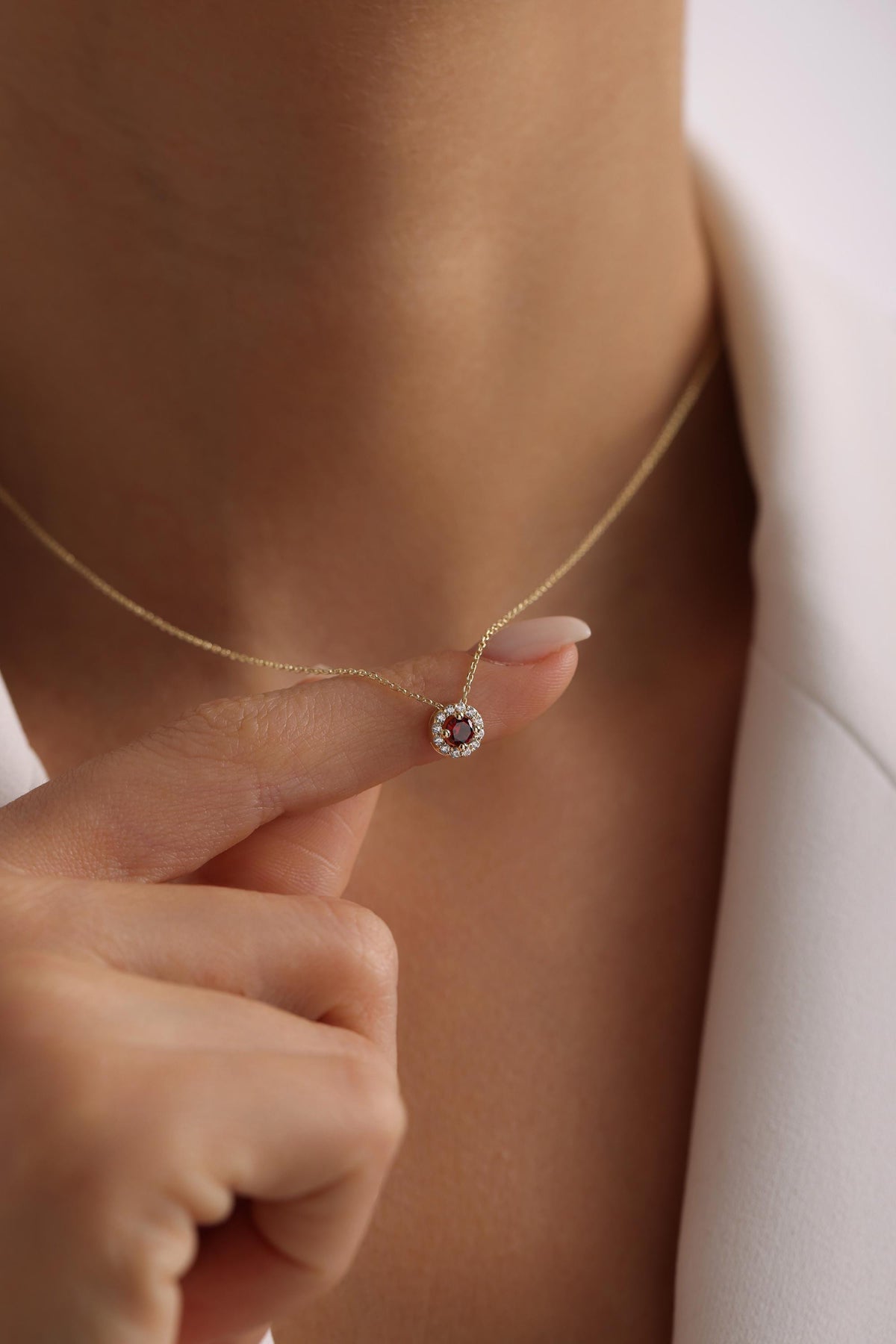 May include: A gold necklace with a small pendant featuring a red gemstone surrounded by a halo of smaller white gemstones.